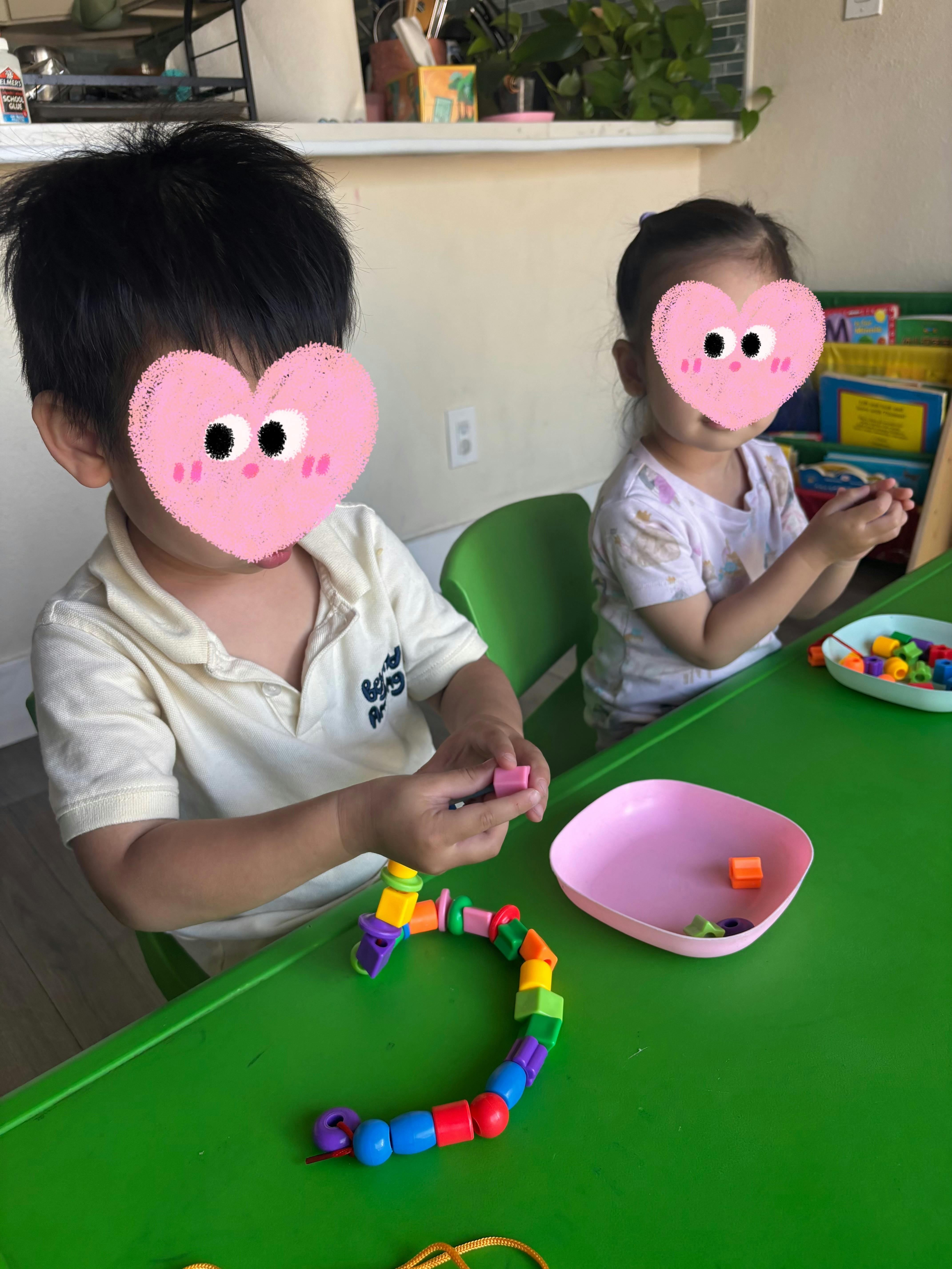 Two children sitting at a table playing with colorful linking beads