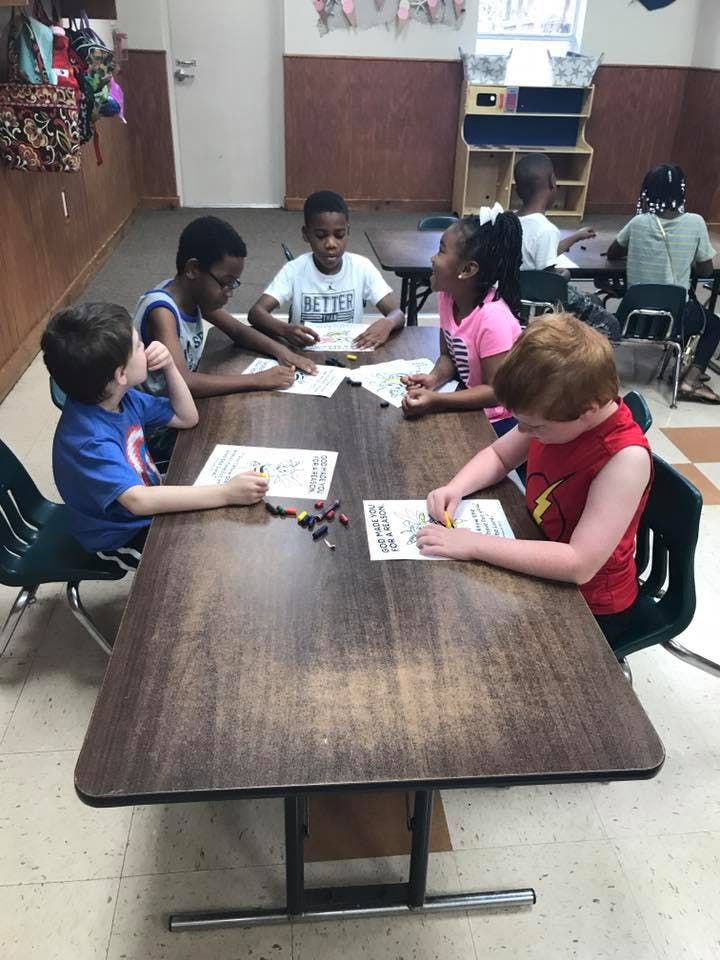 Children sitting at a table coloring on papers