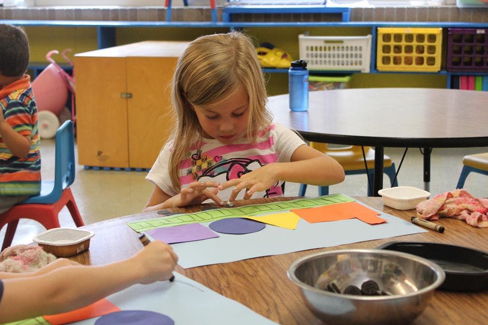 Child working on a craft project at a table in a classroom
