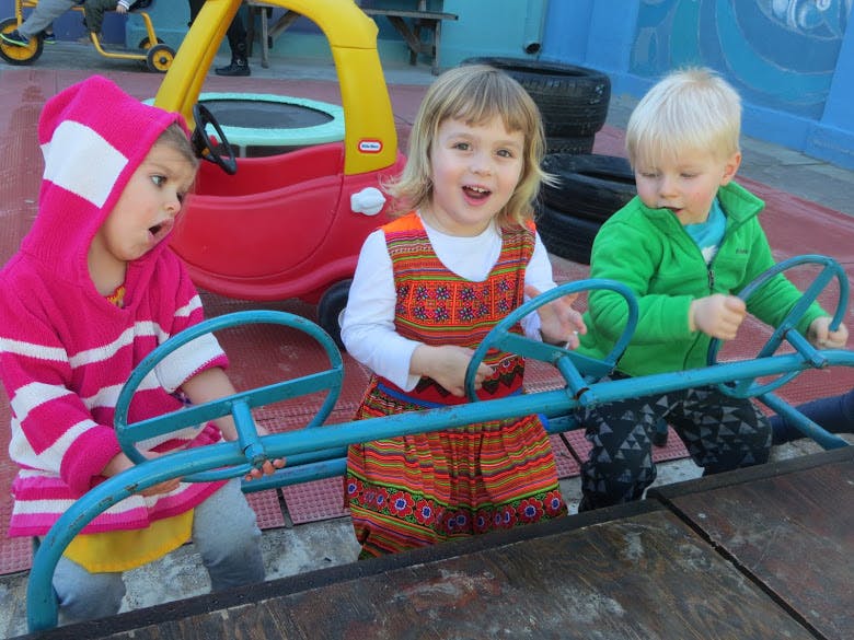 Three children playing on a playground structure with toy steering wheels