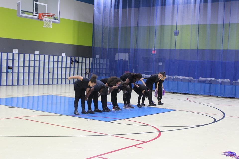 Group of people in black clothing bending forward on a blue mat in a gym