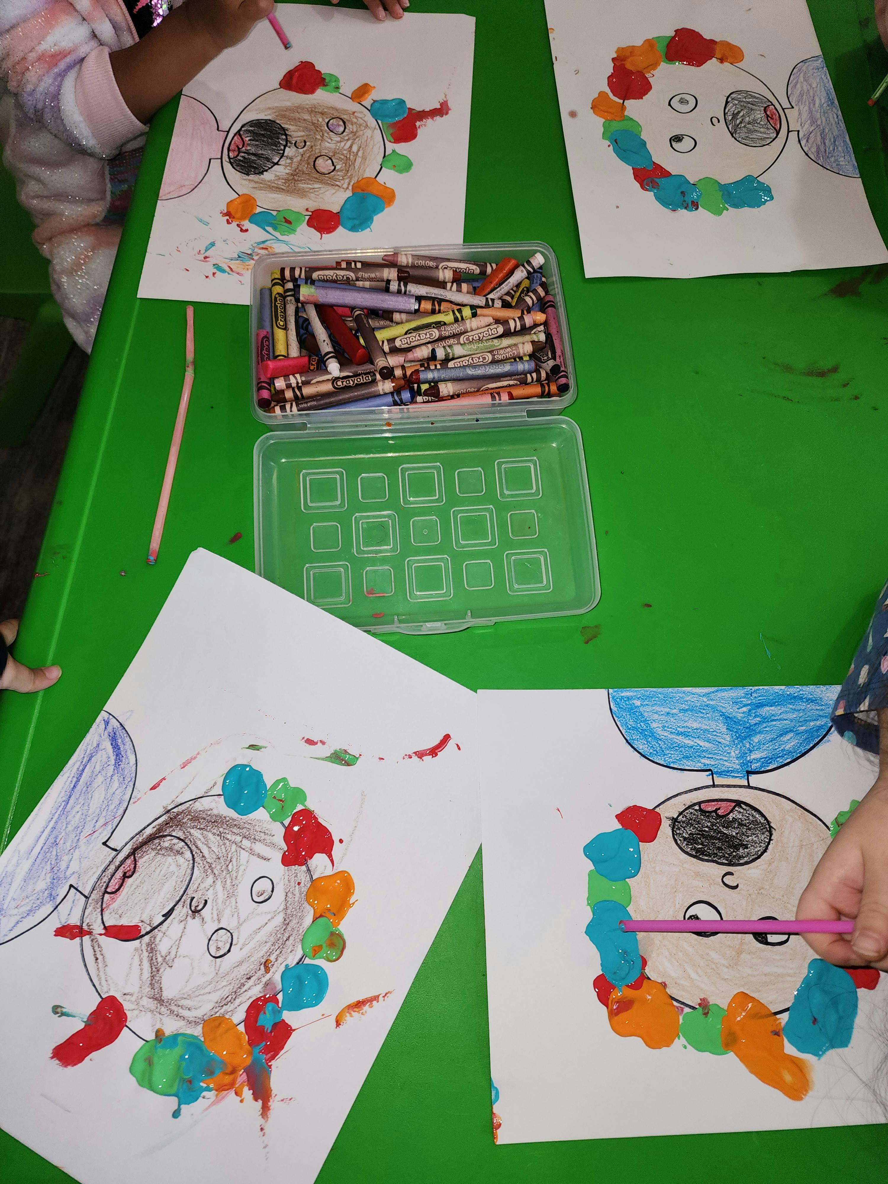 Children's drawings with paint and crayons on a green table