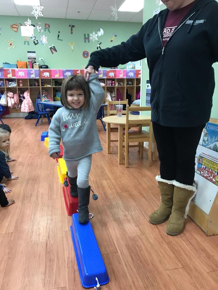 Child walking on colorful balance beams while holding a person's hand