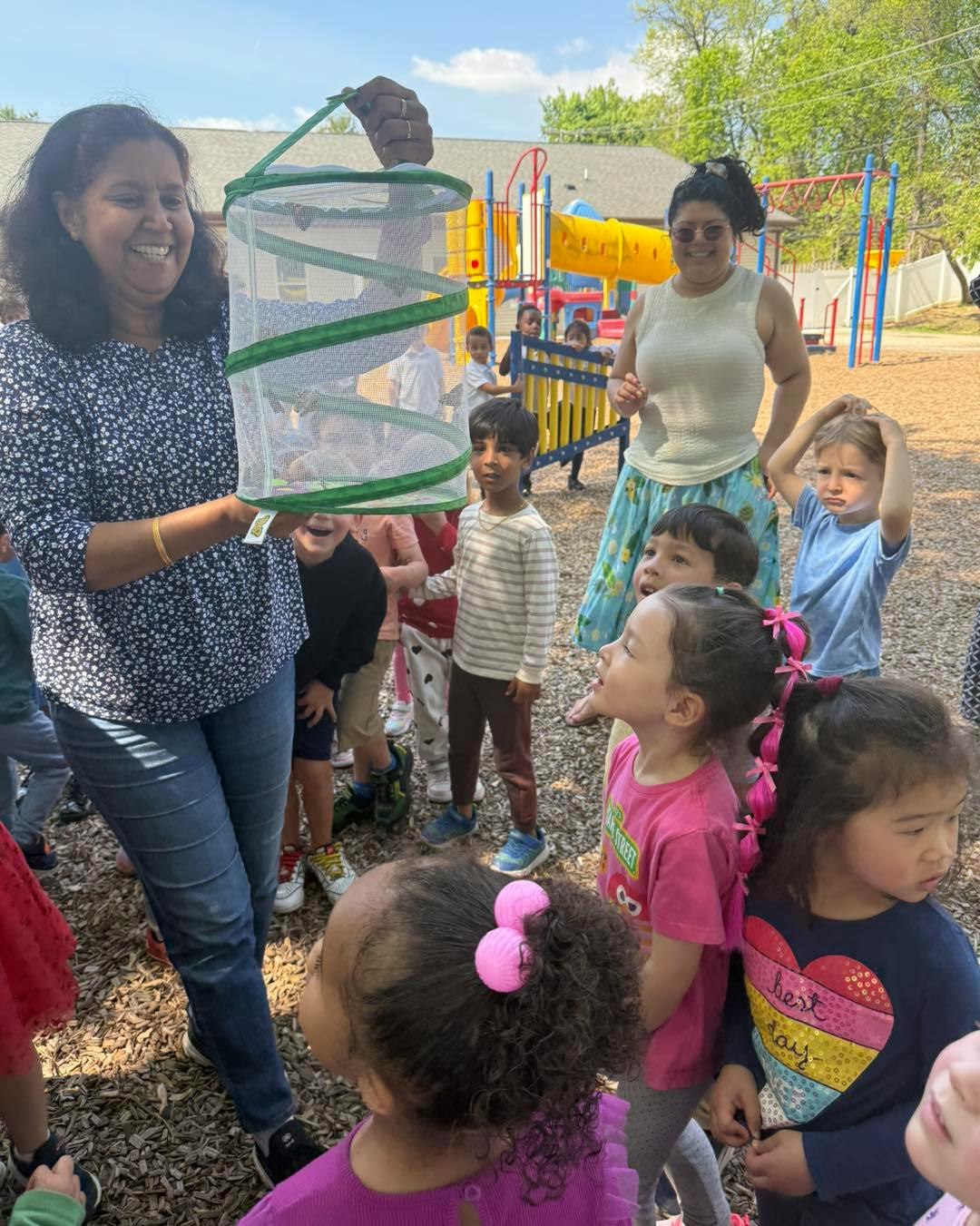 Person holding a butterfly habitat for a group of children outdoors