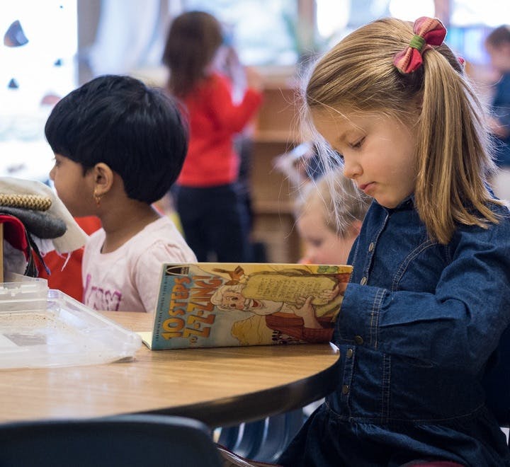 Child in denim shirt reading a book at a table