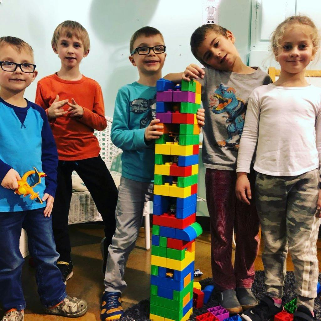 Five children standing around a tall stack of colorful building blocks