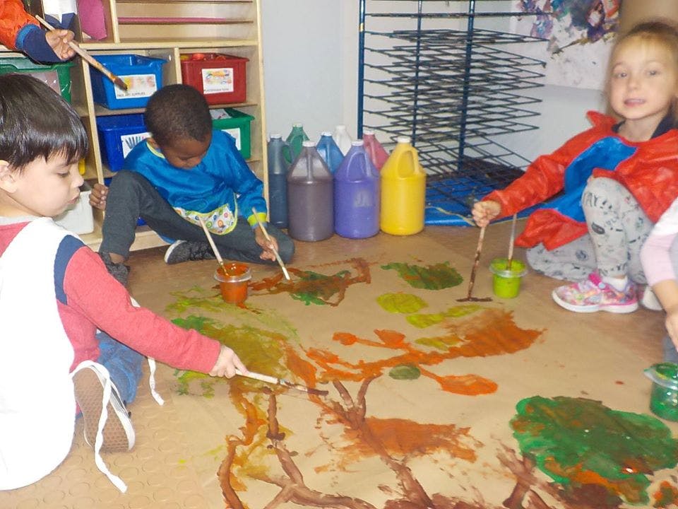 Three children painting on a large sheet of paper on the floor