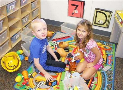 Two children playing with toys on a colorful rug in a classroom