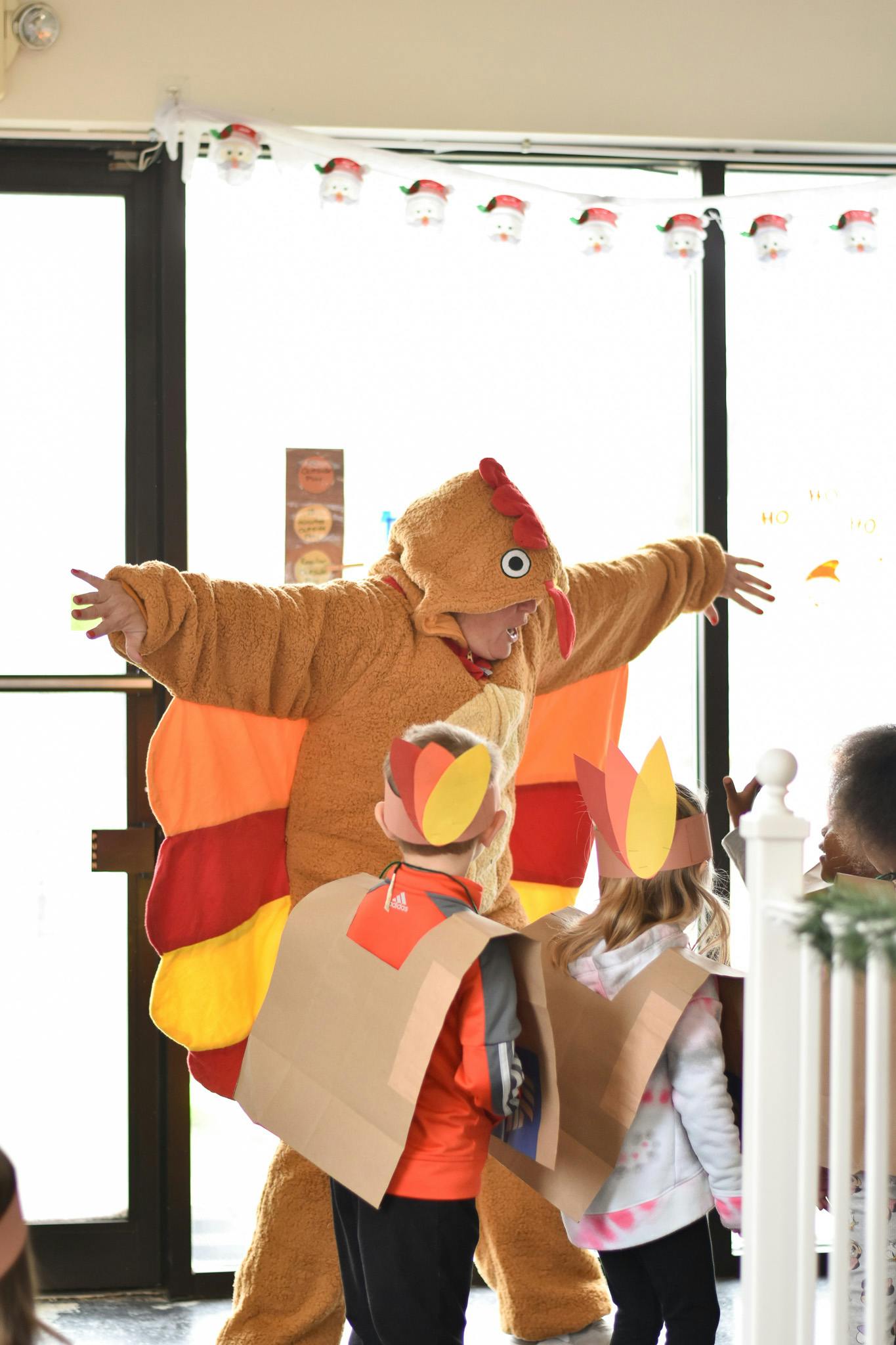 Person in turkey costume with children wearing turkey hats and cardboard feathers