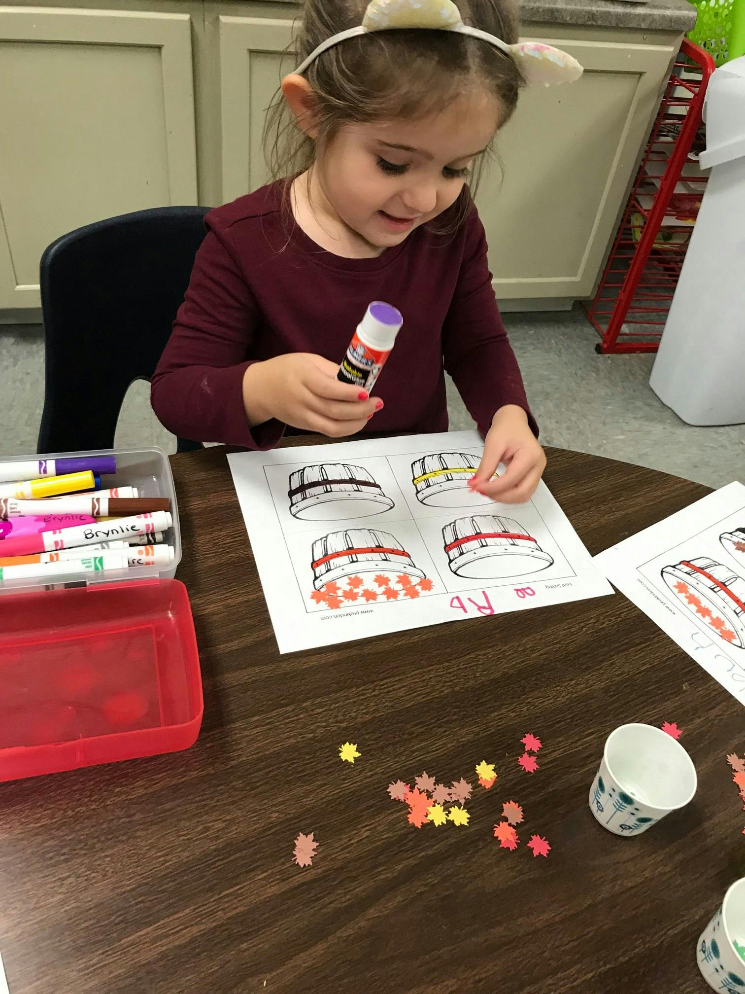 Child holding a glue stick and crafting with paper cutouts