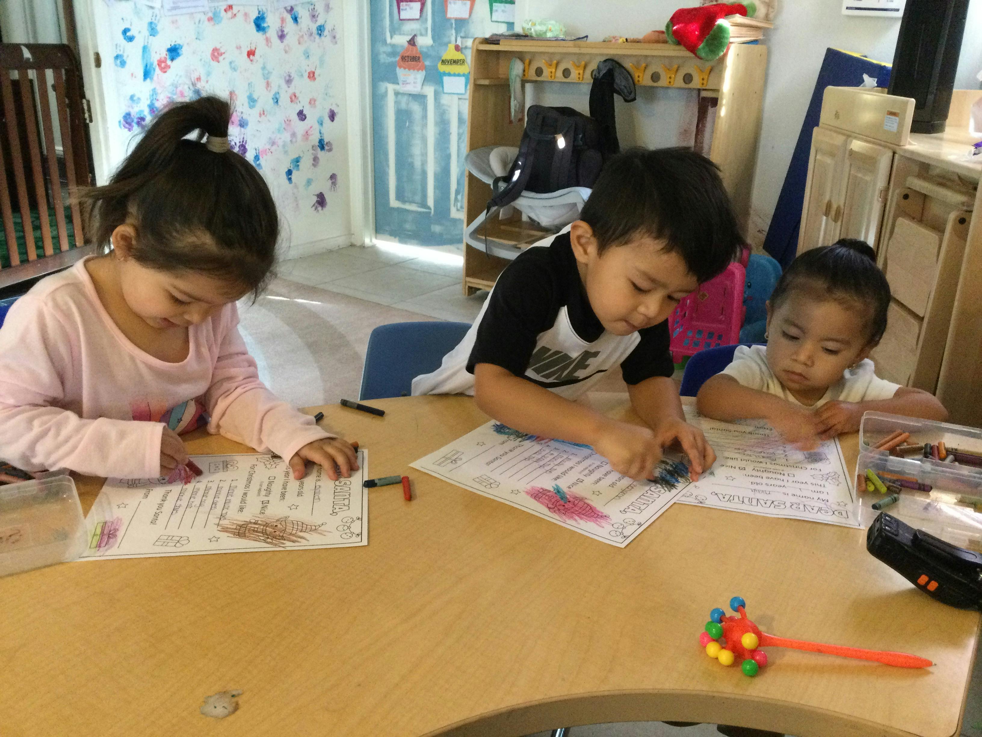 Three children coloring at a table in a classroom