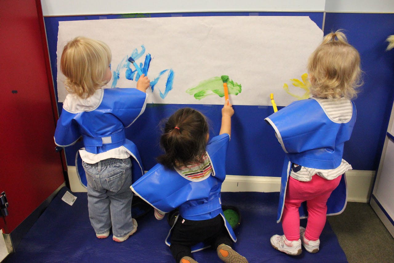 Three children in smocks painting on a wall
