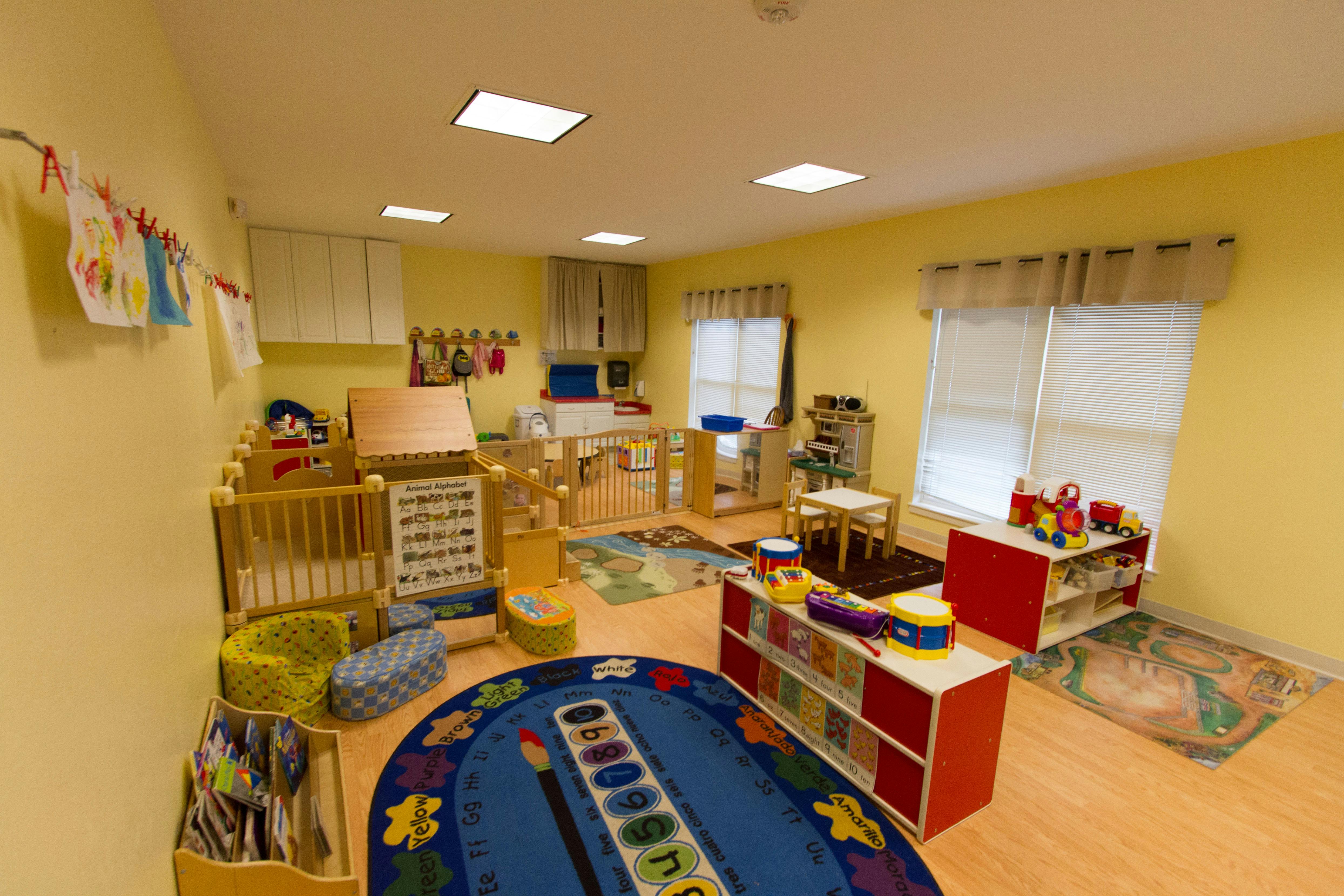 Daycare room with cribs, play mats, and shelves of toys