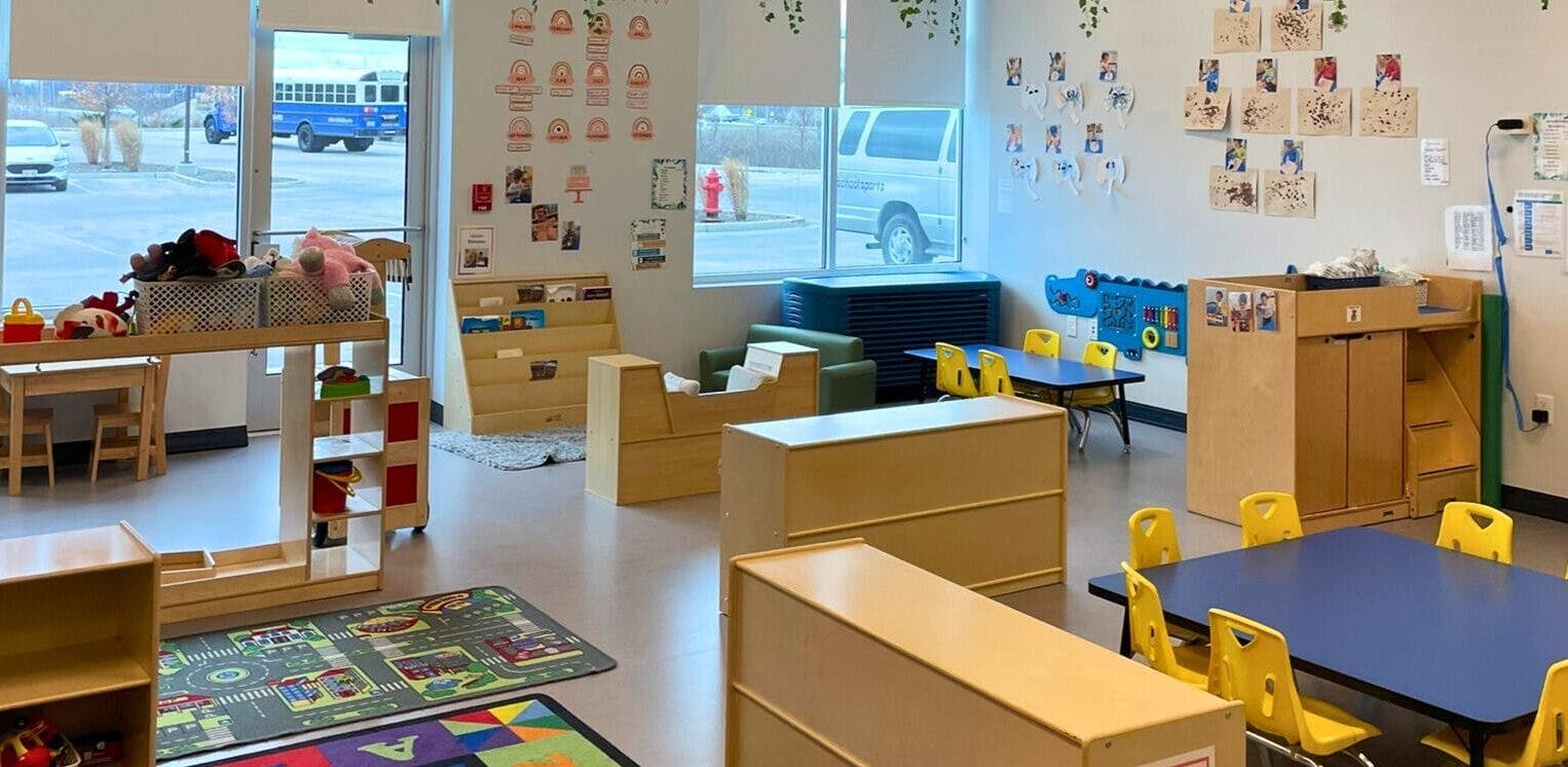 An empty early learning classroom with small tables, chairs, and shelves