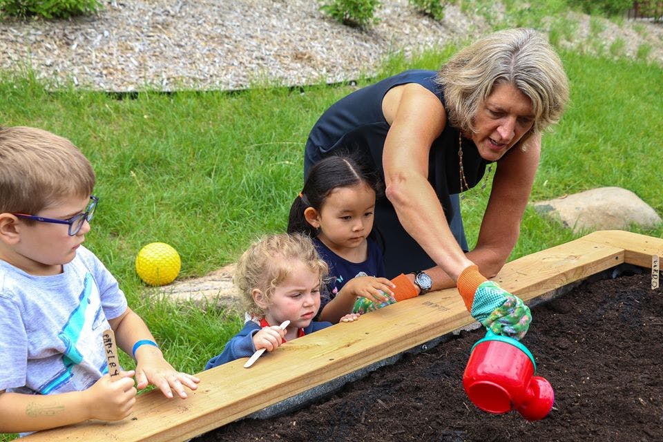 Adult and three children planting in a raised garden bed