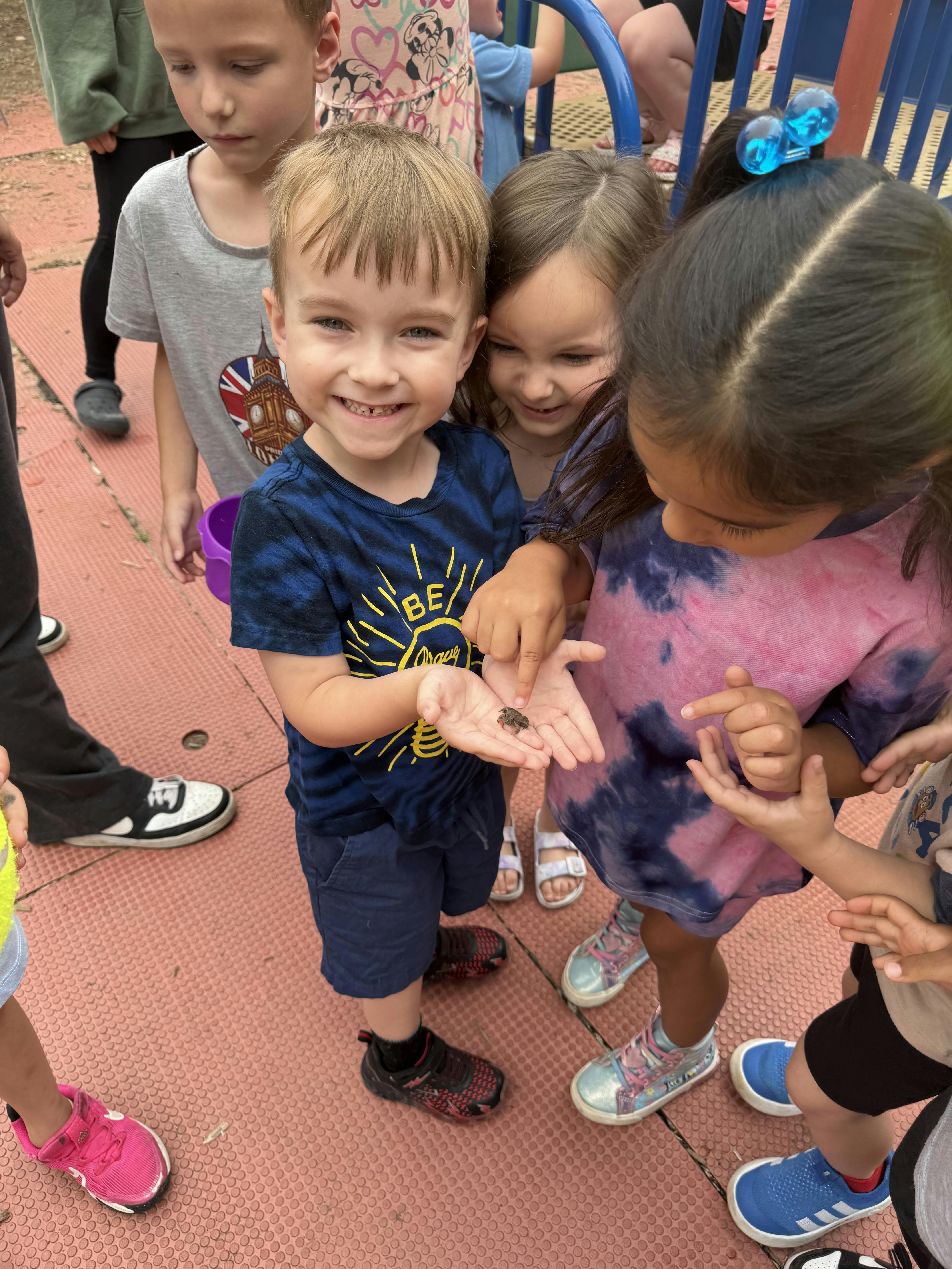 Child holding an insect in their hand, surrounded by other children looking