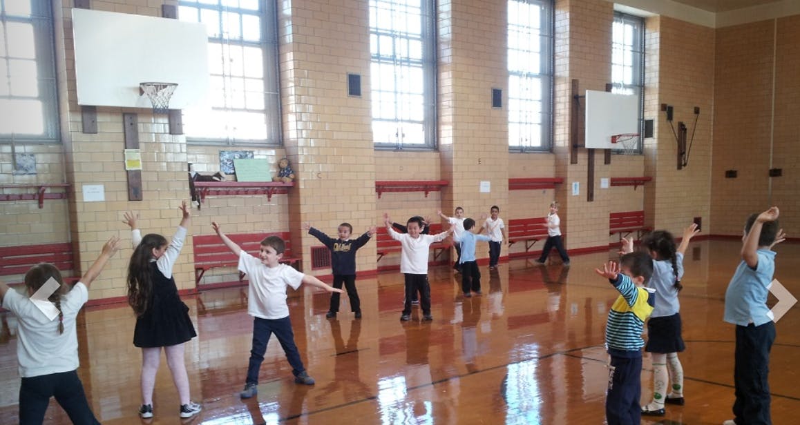Children in a gymnasium with arms raised