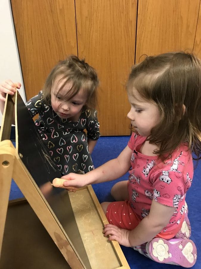 Two children playing with a wooden ramp and black easel