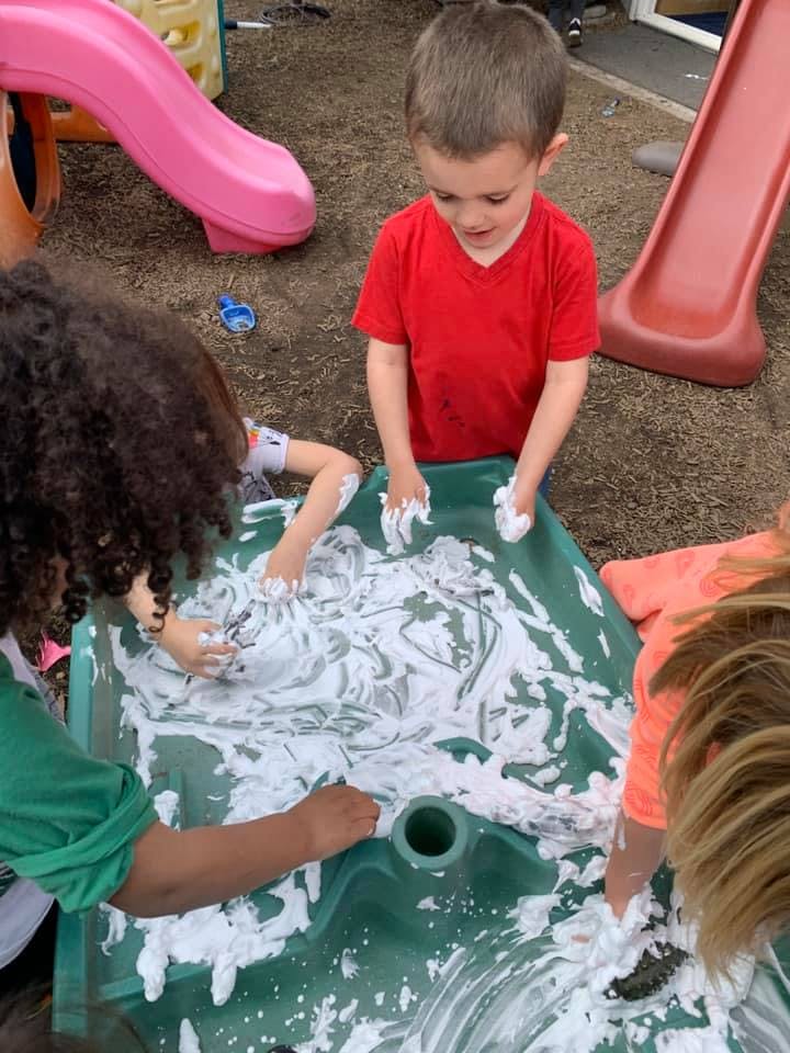 Children playing with shaving cream in a green sensory bin