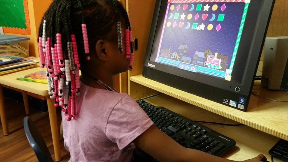 Child with beaded braids looking at a computer screen with a game