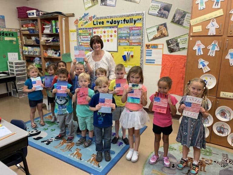 Adult and children holding up paper American flags in a classroom