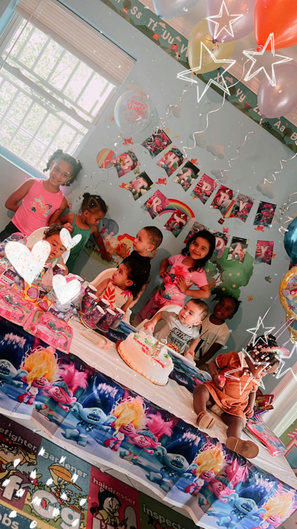 Children gathered around a table with a cake and balloons