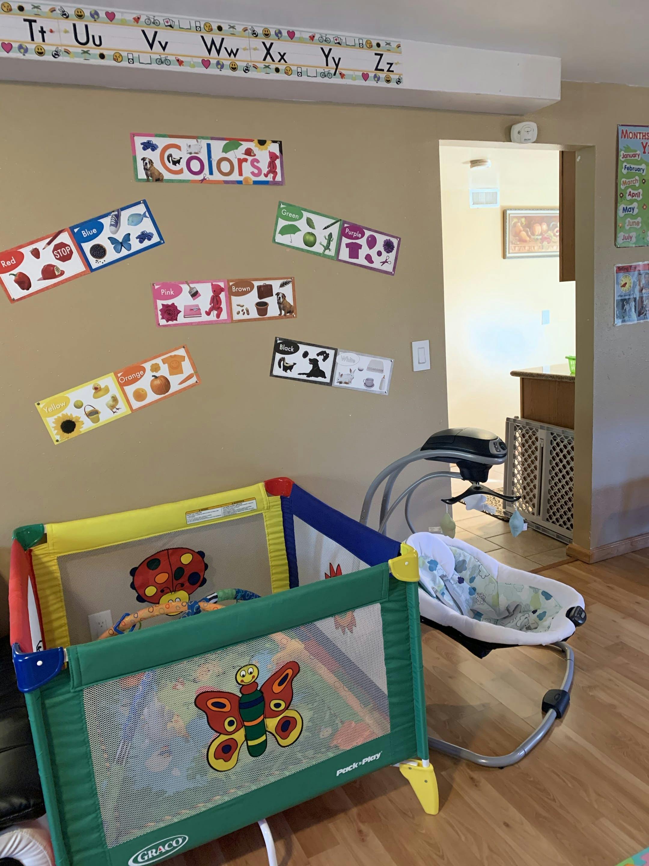Playpen and baby bouncer in a room with educational posters on the wall