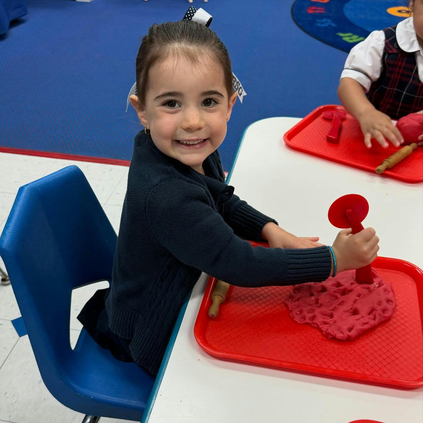 Child playing with red playdough and toy pizza cutter at a table