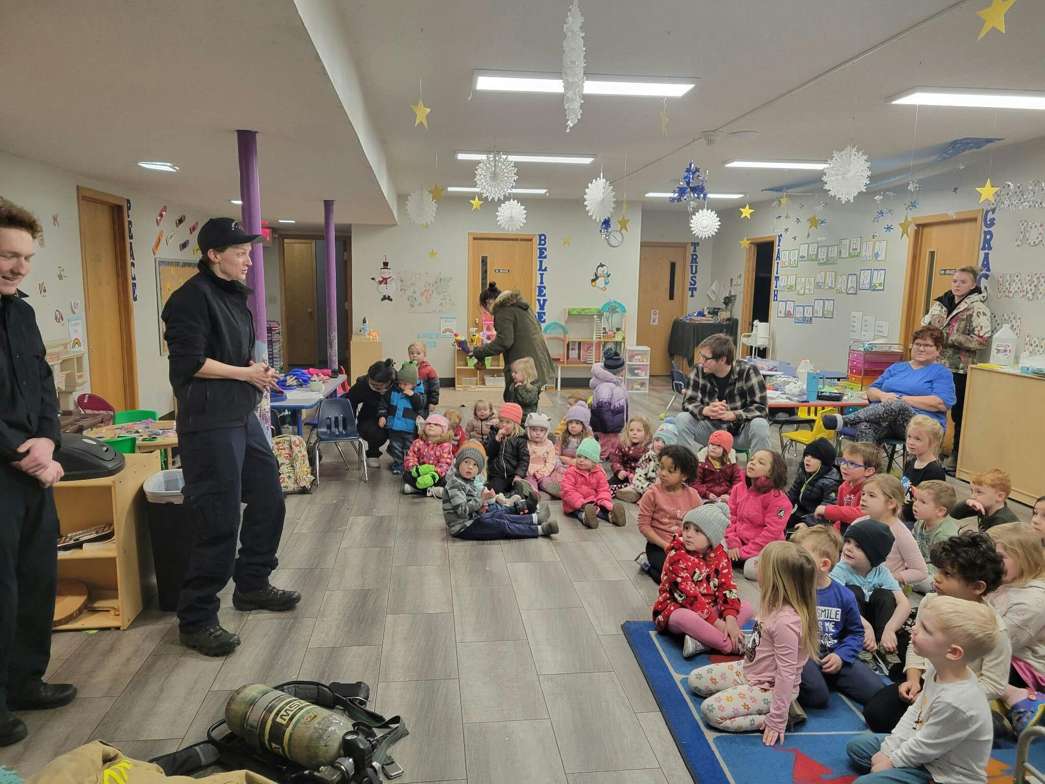 Two people standing in front of a group of children sitting on the floor