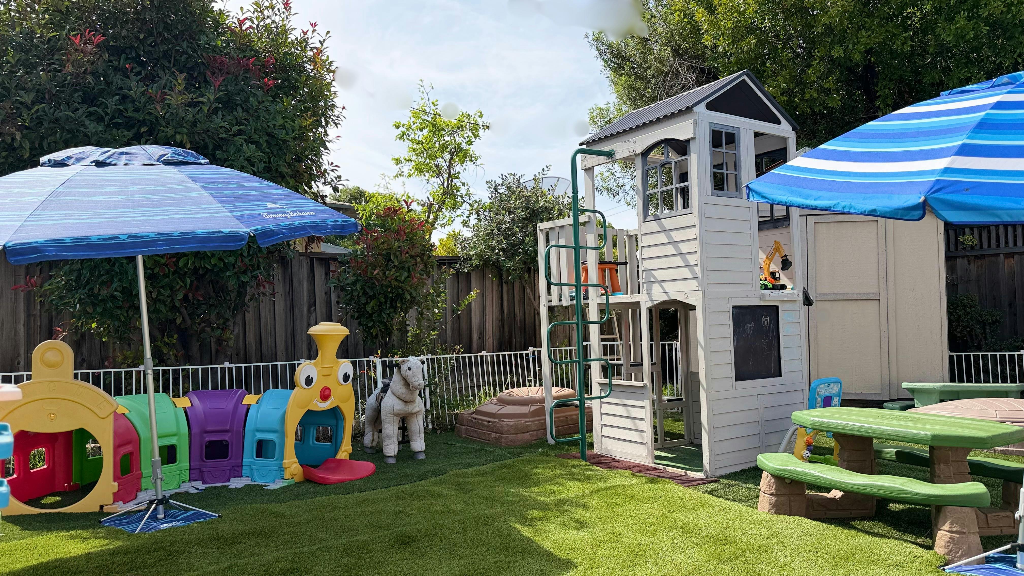 backyard play area with a playhouse, slide, plastic train, and picnic tables