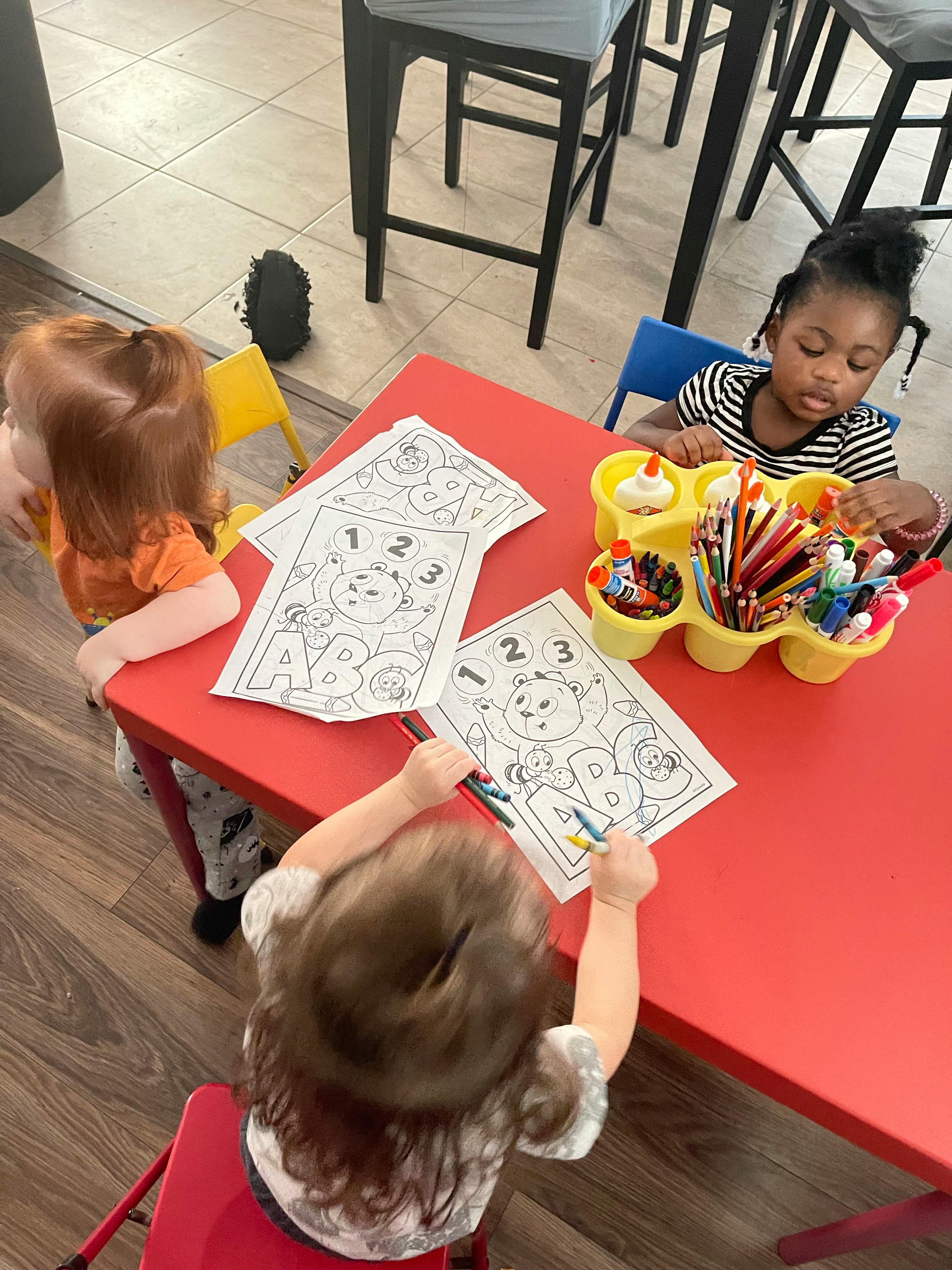 Three children coloring at a red table
