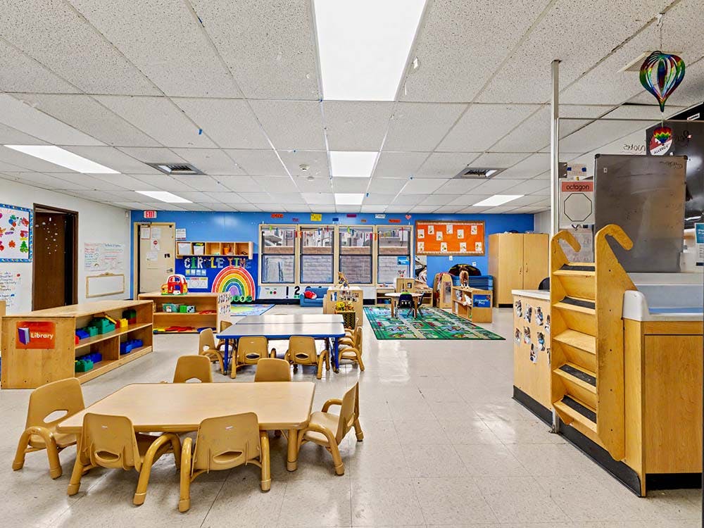 Classroom with small tables and chairs, shelves, and a rainbow wall decoration