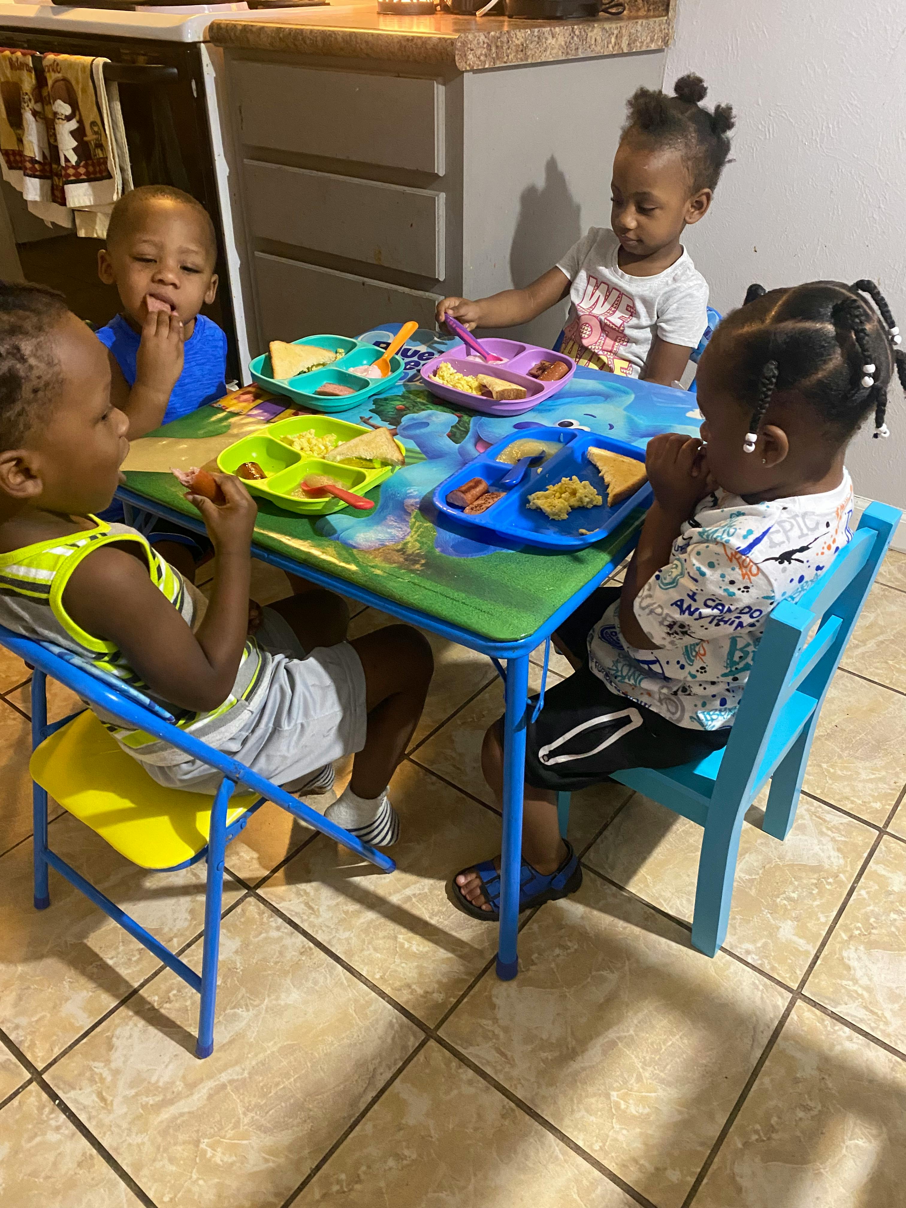 Four children eating at a small table in a kitchen