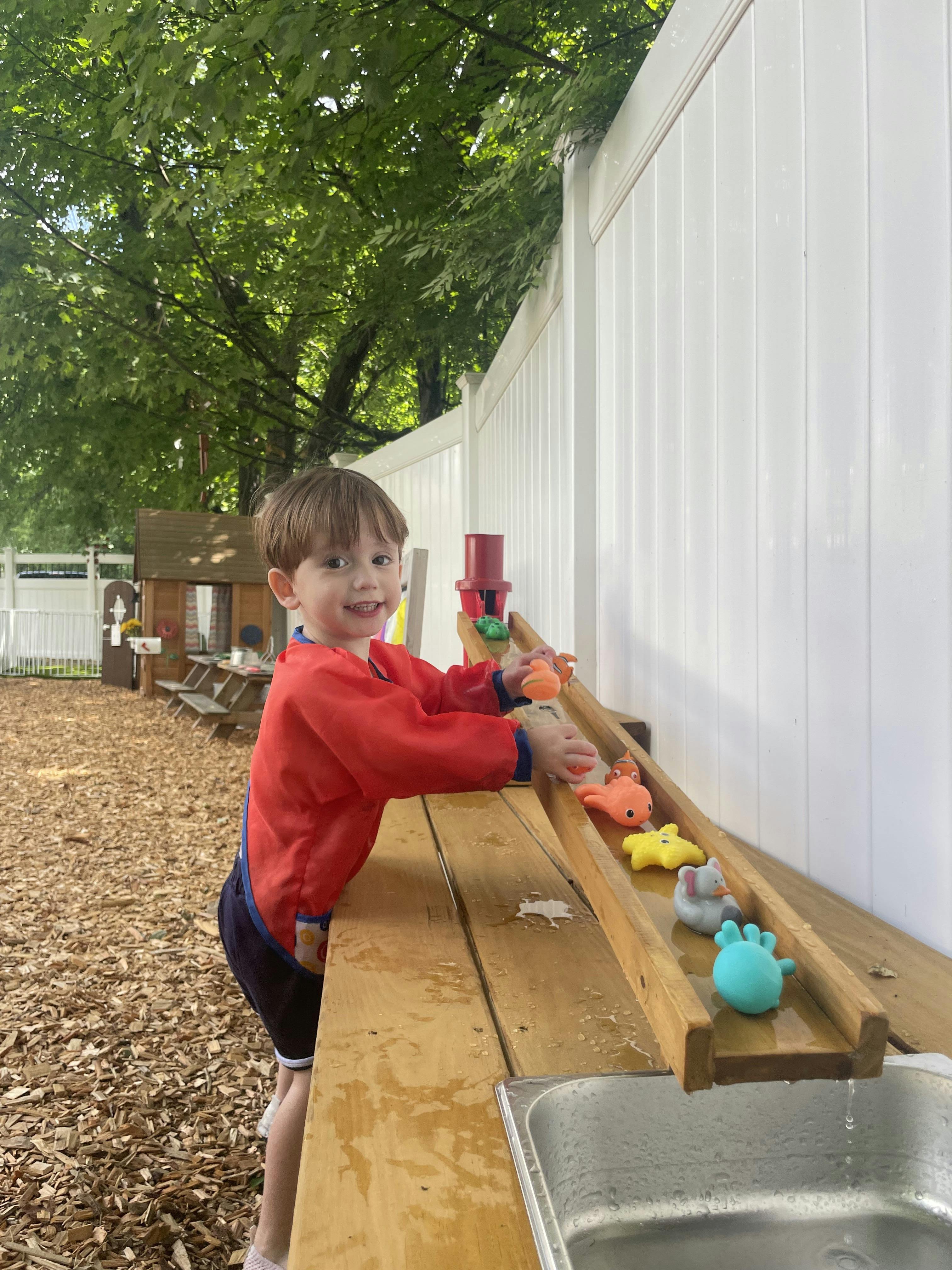 Child playing with water toys on a wooden ramp leading to a sink
