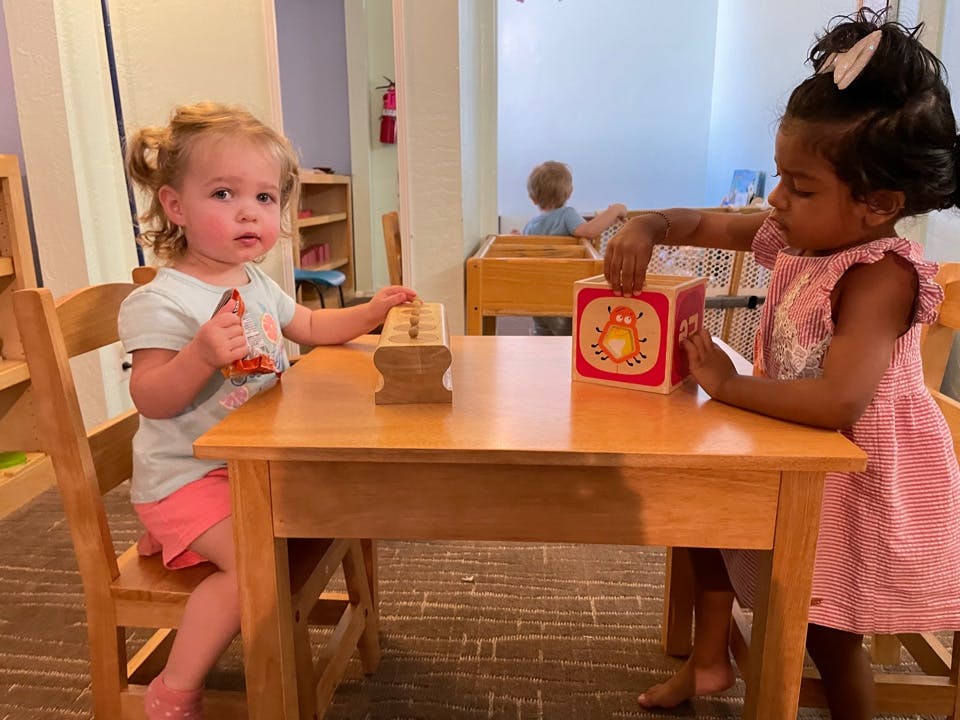 Two children playing with toys at a table in a classroom