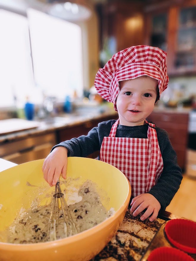 Child in chef hat and apron mixing batter in a large bowl with a whisk