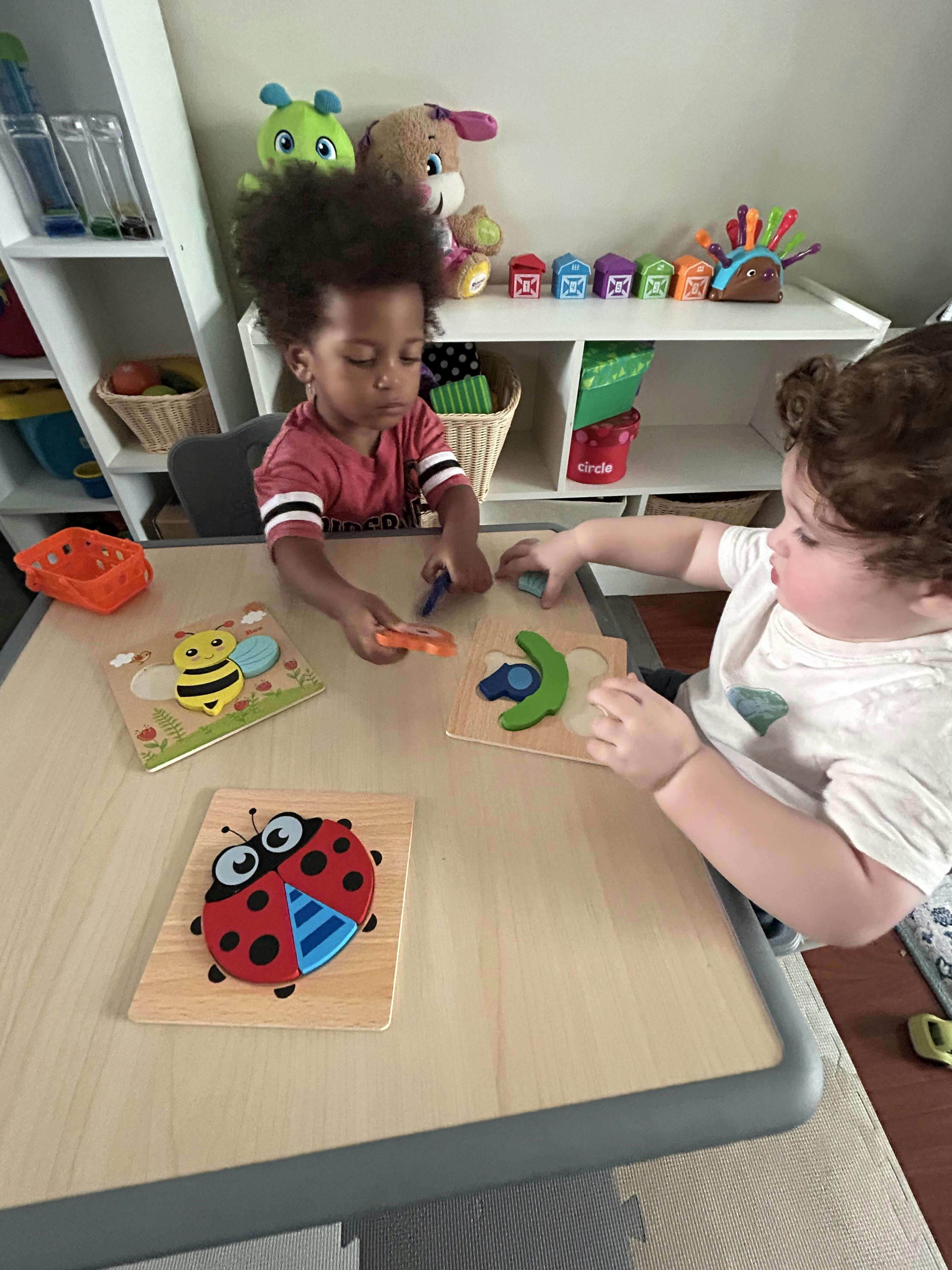Two children playing with wooden puzzles at a table