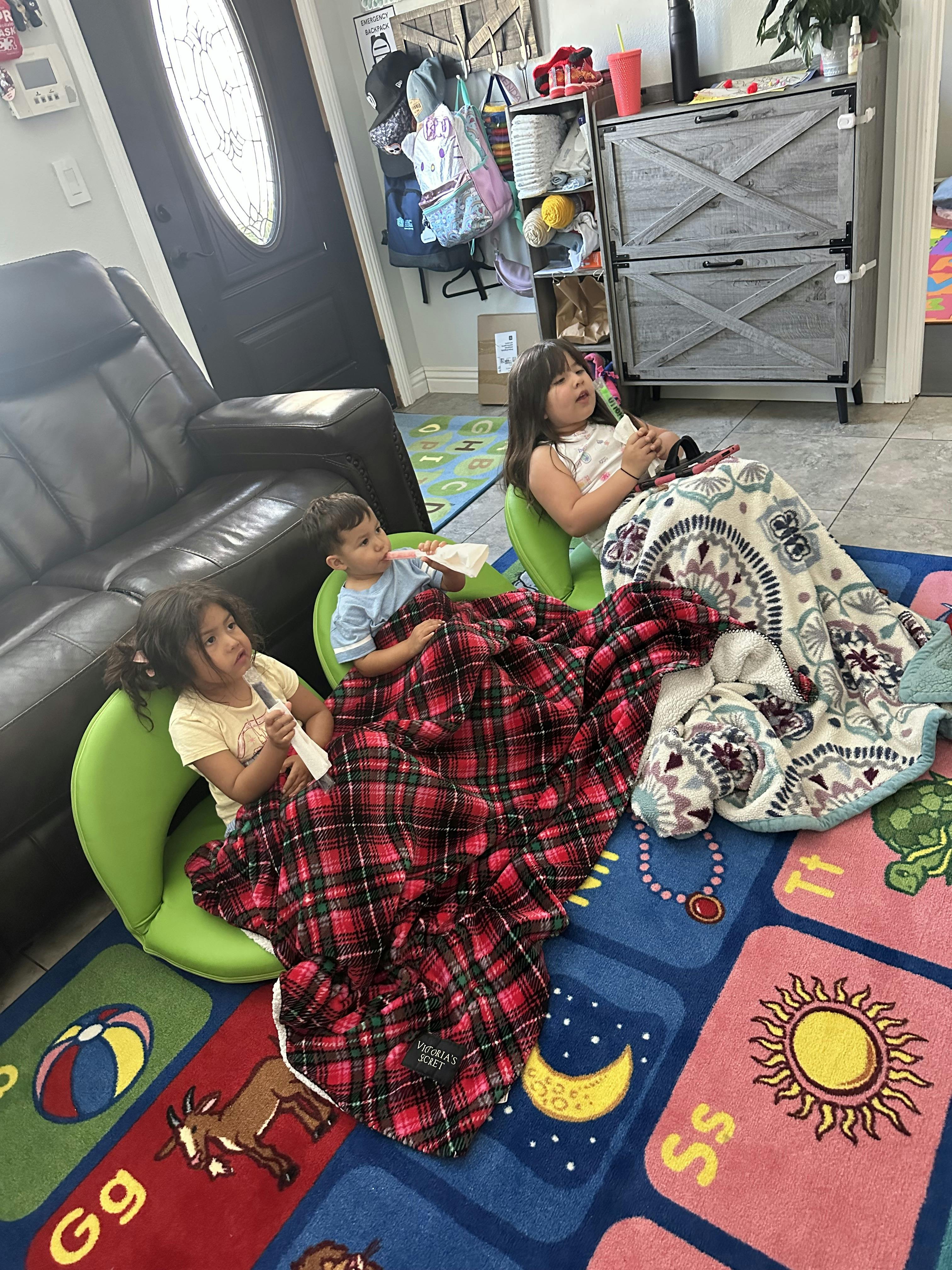 Three children sitting on the floor with blankets in a living room