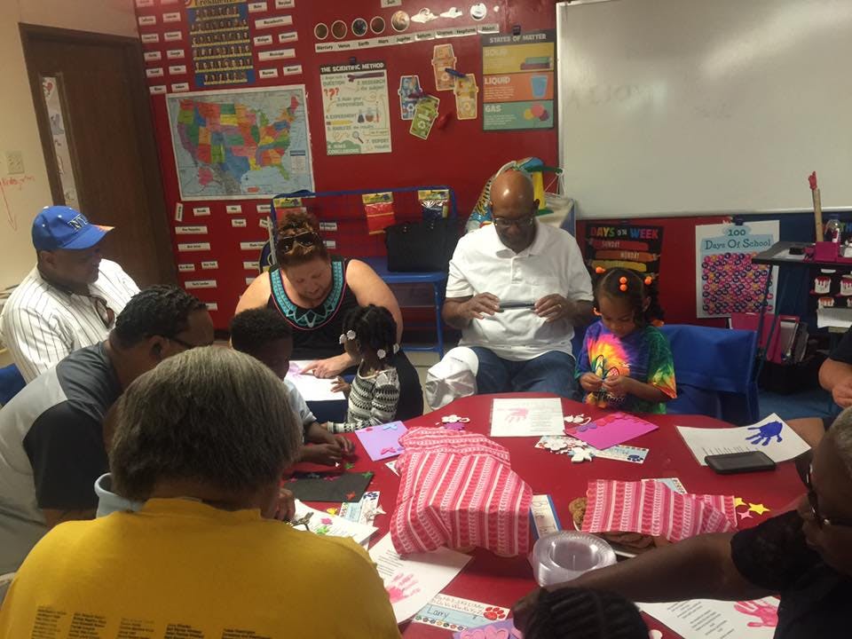 People and children sitting around a table doing crafts in a classroom