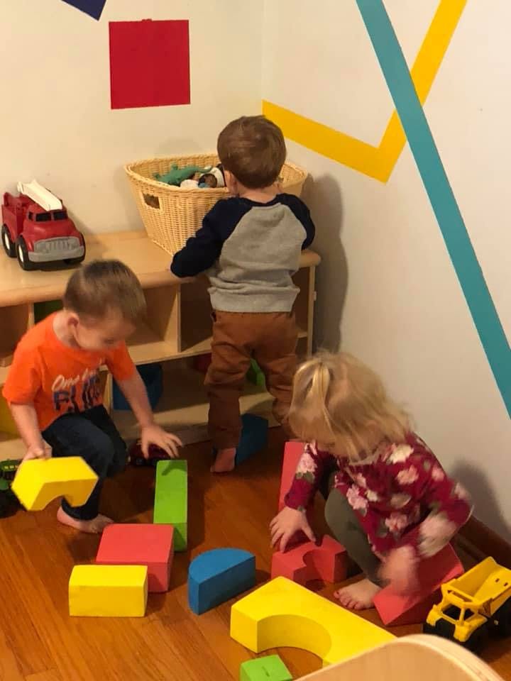 Three children playing with colorful building blocks on a wooden floor