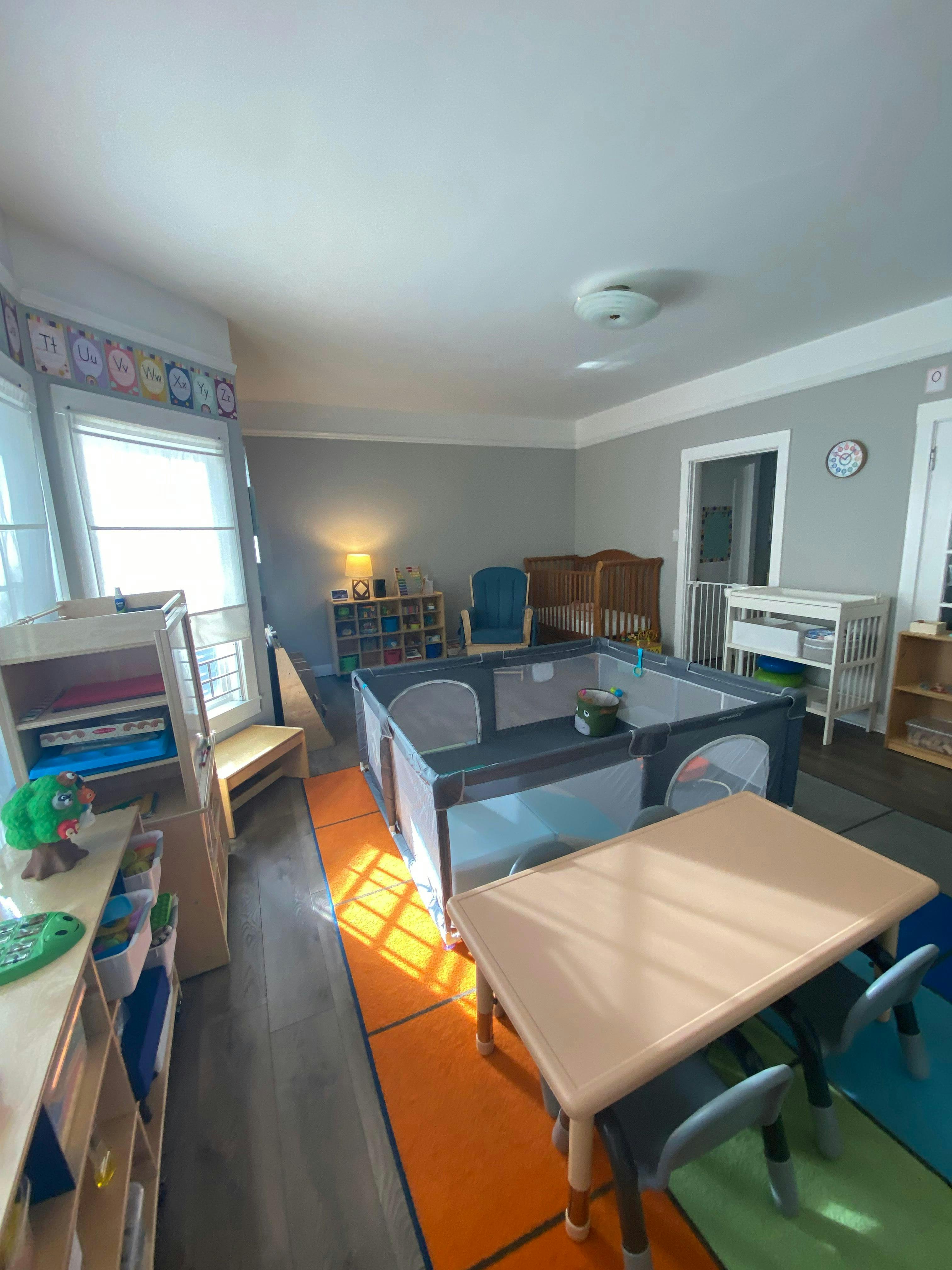 Playpen and small table with chairs in a room with cribs and shelves