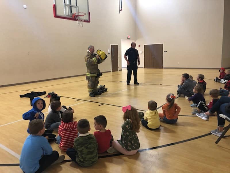 Firefighter showing equipment to children sitting on a gym floor