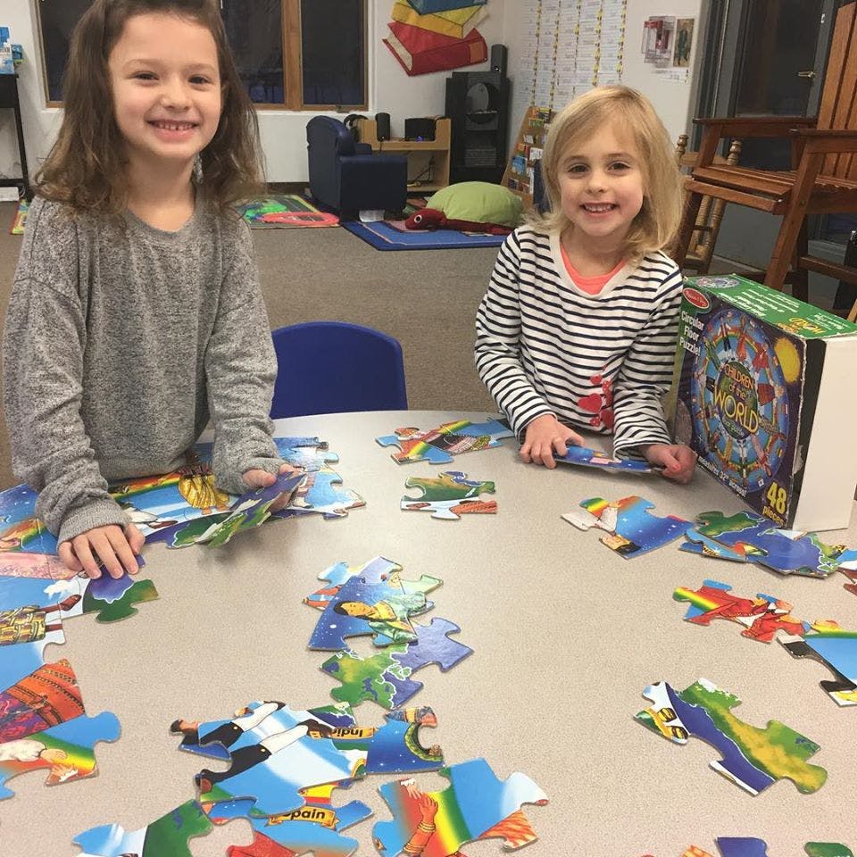 Two children sitting at a table with puzzle pieces