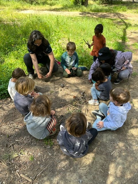 Adults and children sitting in a circle on the ground outdoors
