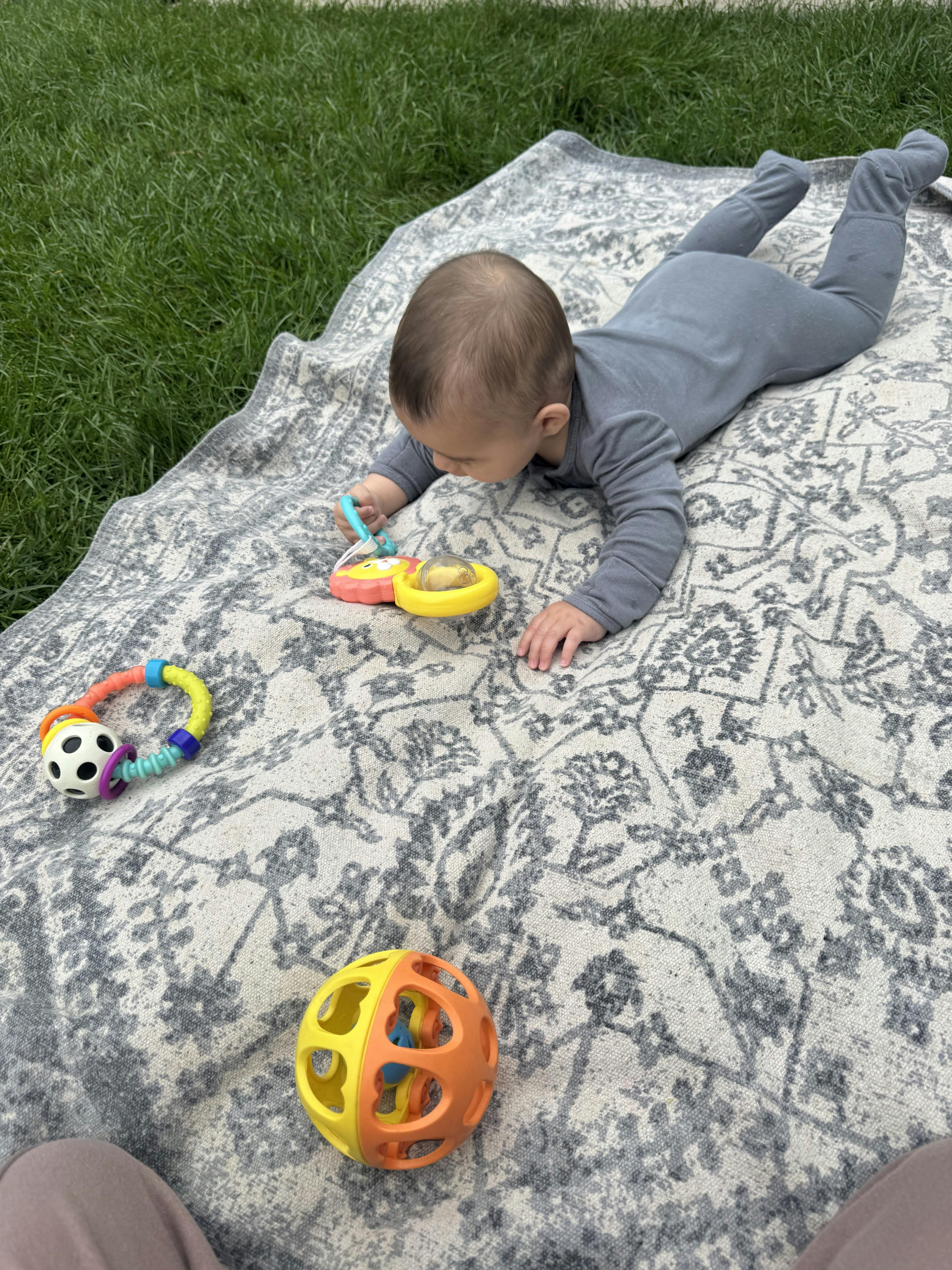 Baby lying on a blanket on the grass playing with toys