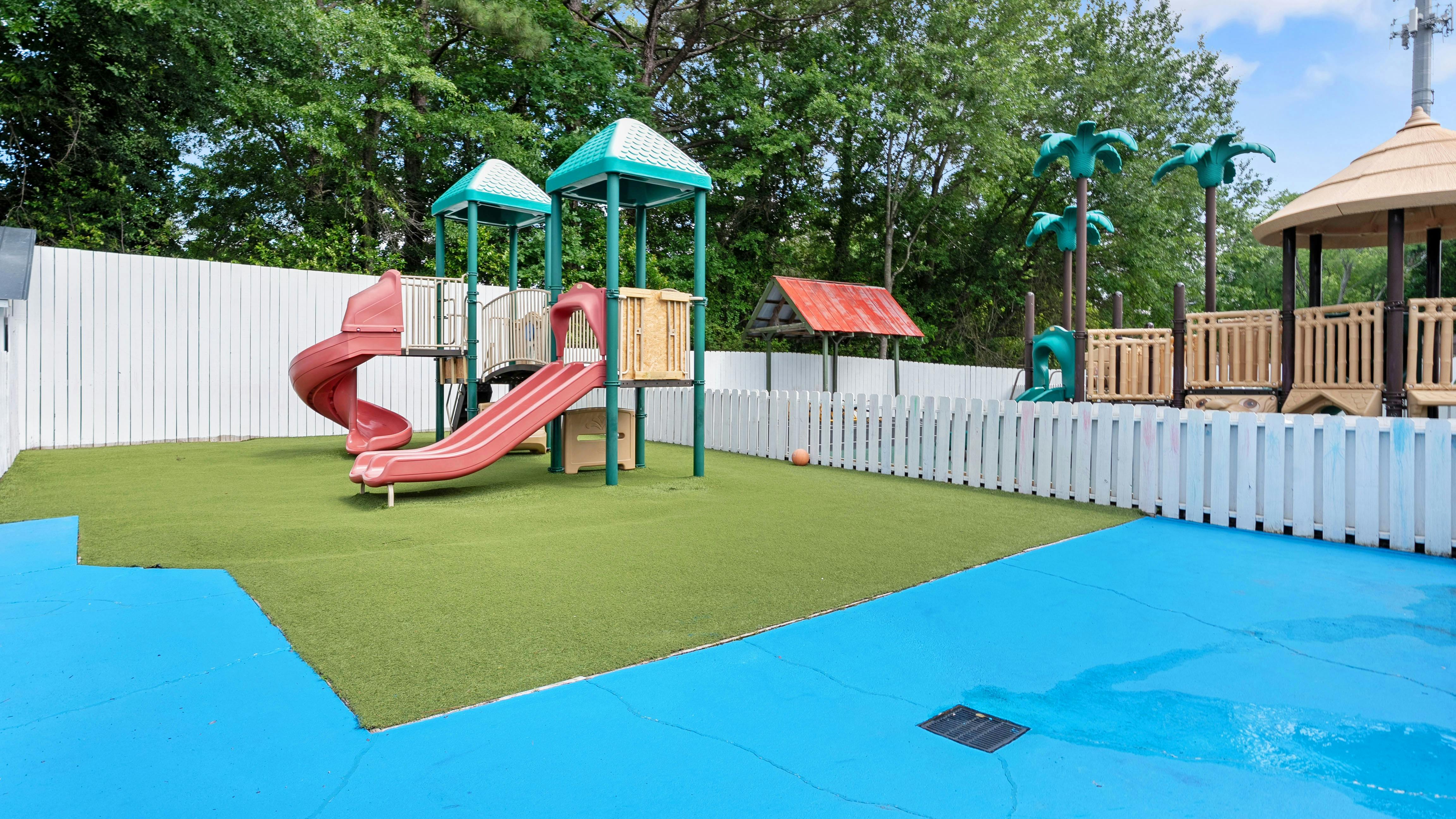 Outdoor playground with red slides, green artificial grass, and blue safety flooring