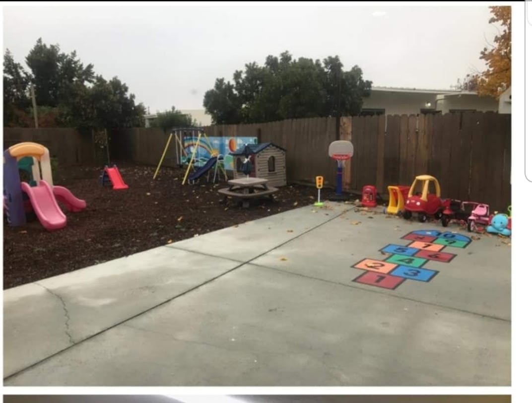 Outdoor play area with slides, swings, playhouse, and hopscotch on concrete