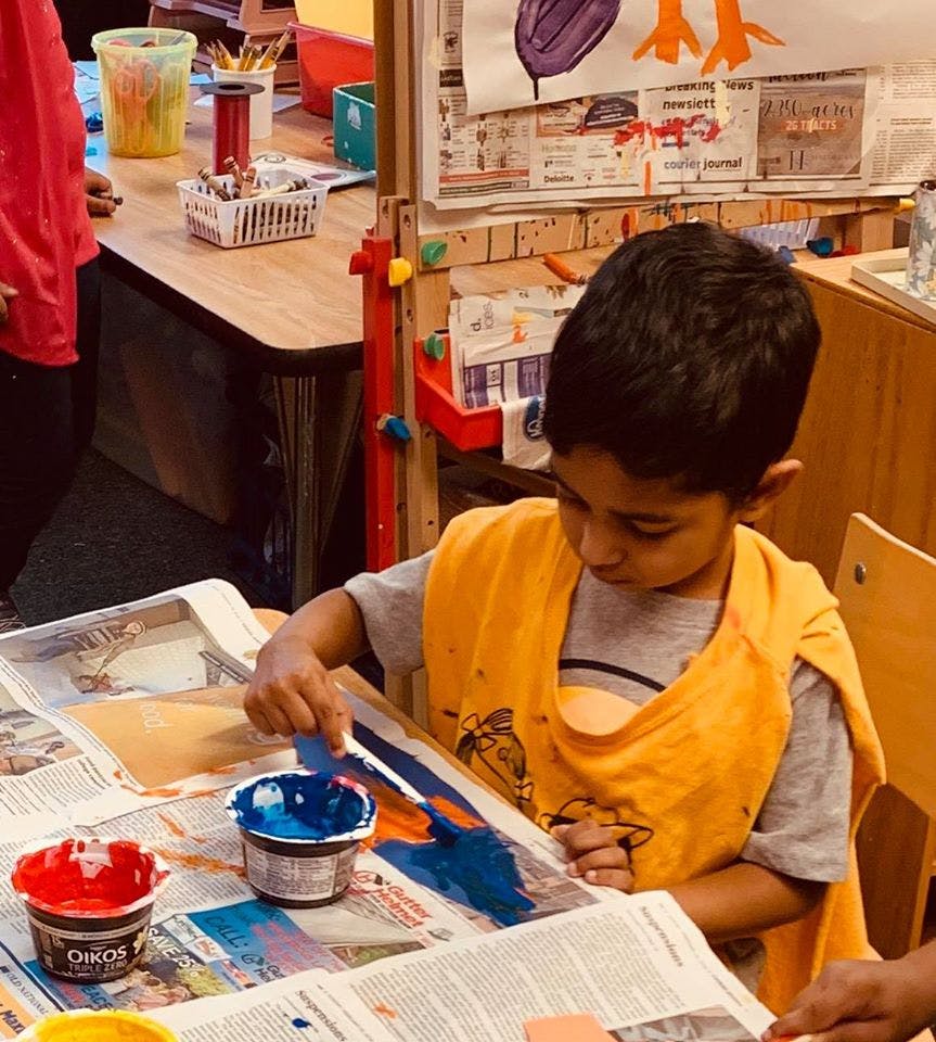 Child painting with blue and orange paint on newspaper in a classroom
