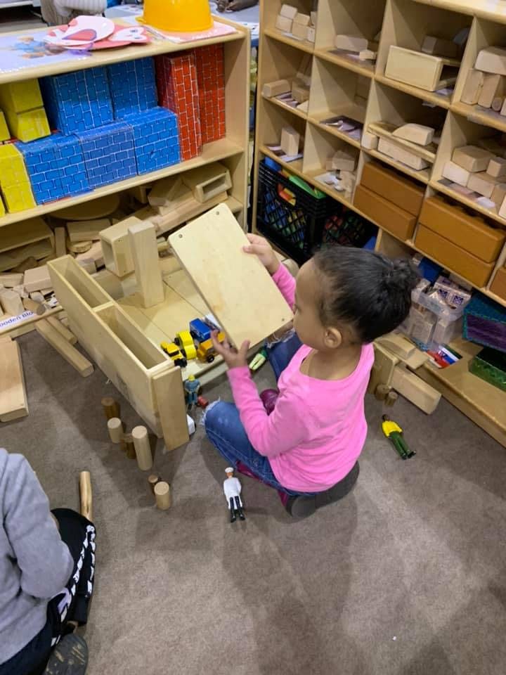 Child playing with wooden blocks and toy trucks on the floor