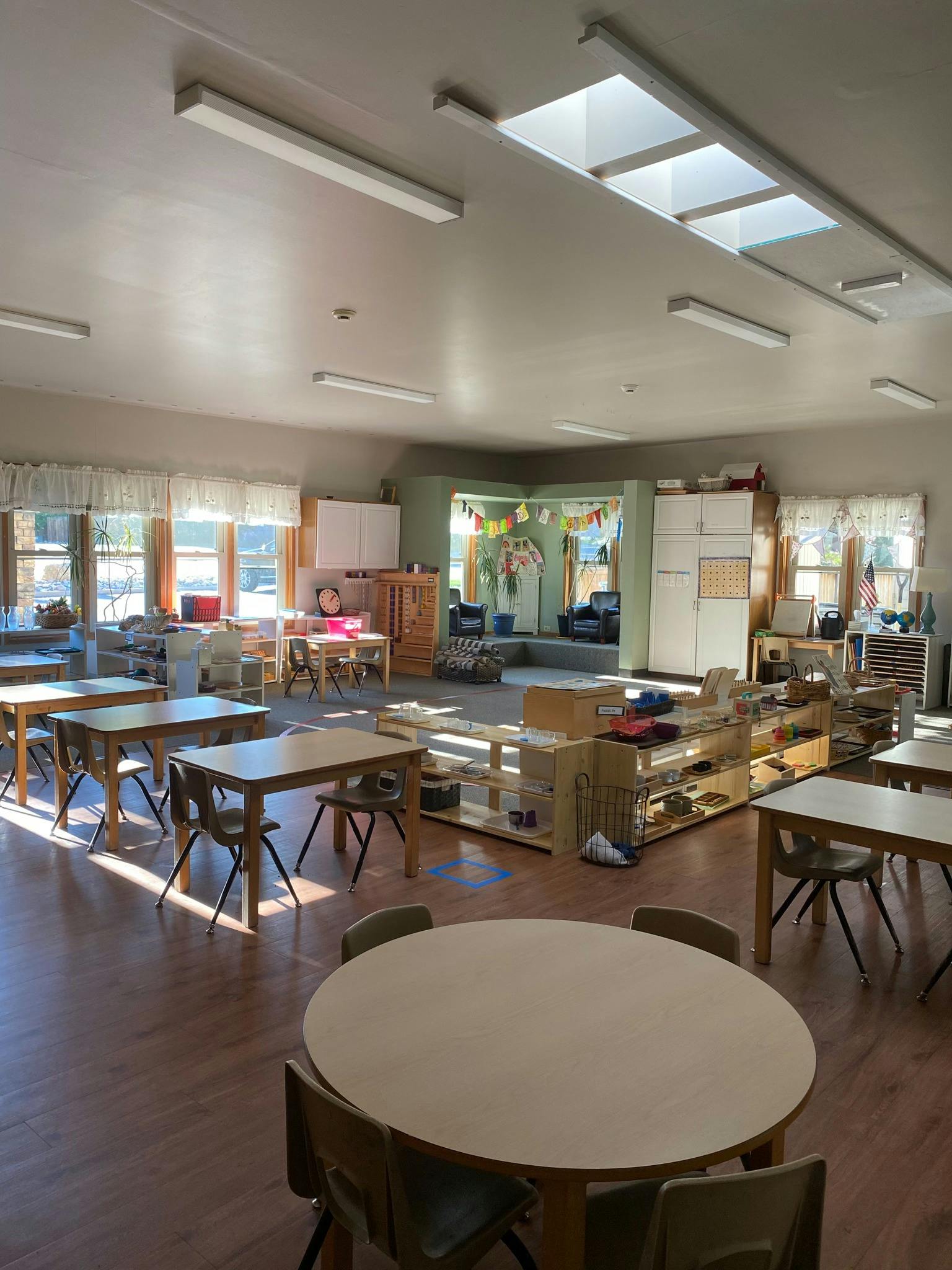 Empty classroom with small tables and chairs, shelves with learning materials